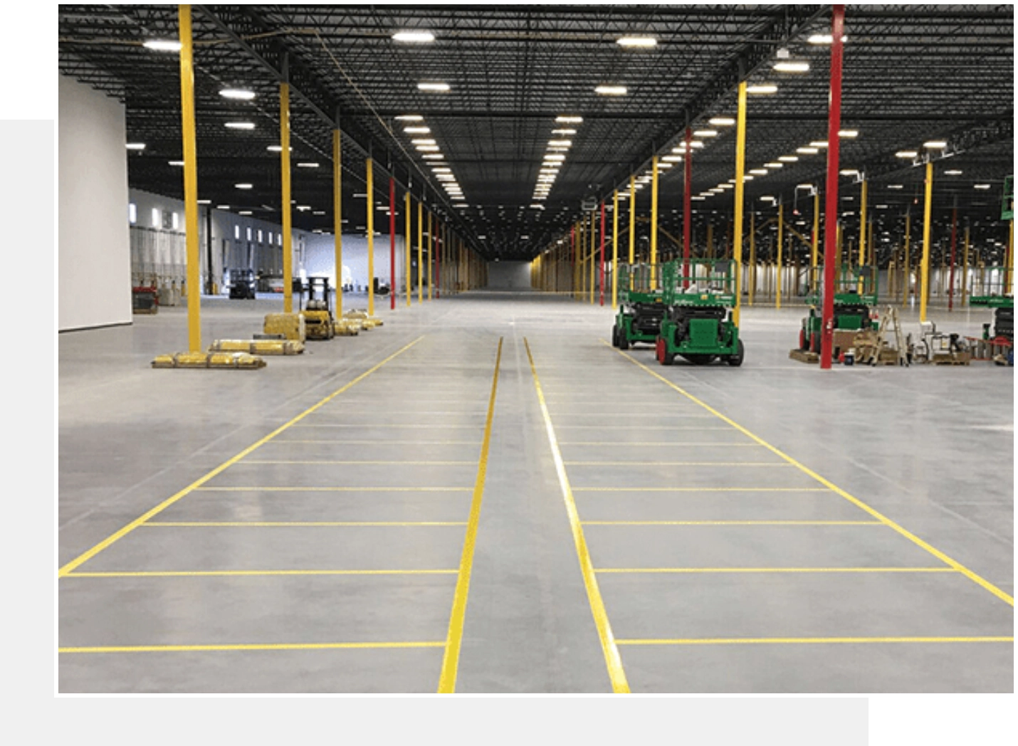 Here's an 8-word alt tag for the image: "Spacious warehouse interior with yellow floor markings and equipment."