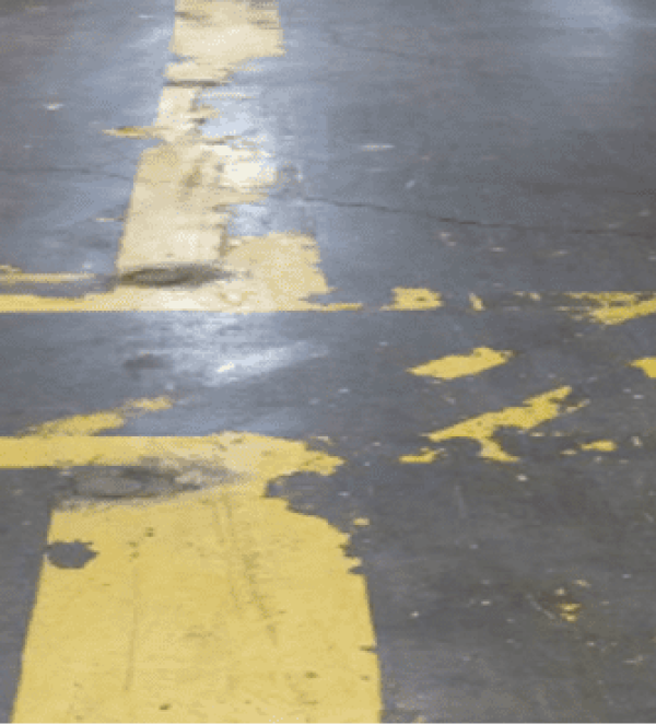 Here's an alt tag for the image: `Damaged yellow parking lines on asphalt`